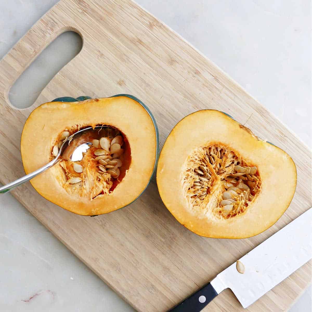acorn squash cut in half on a cutting board with spoon scooping out seeds