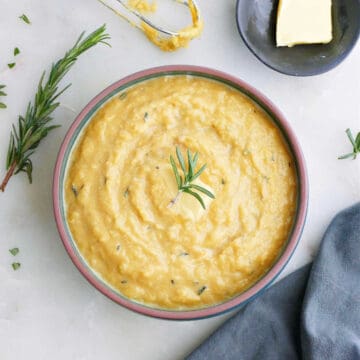 mashed acorn squash topped with rosemary in a bowl on a counter