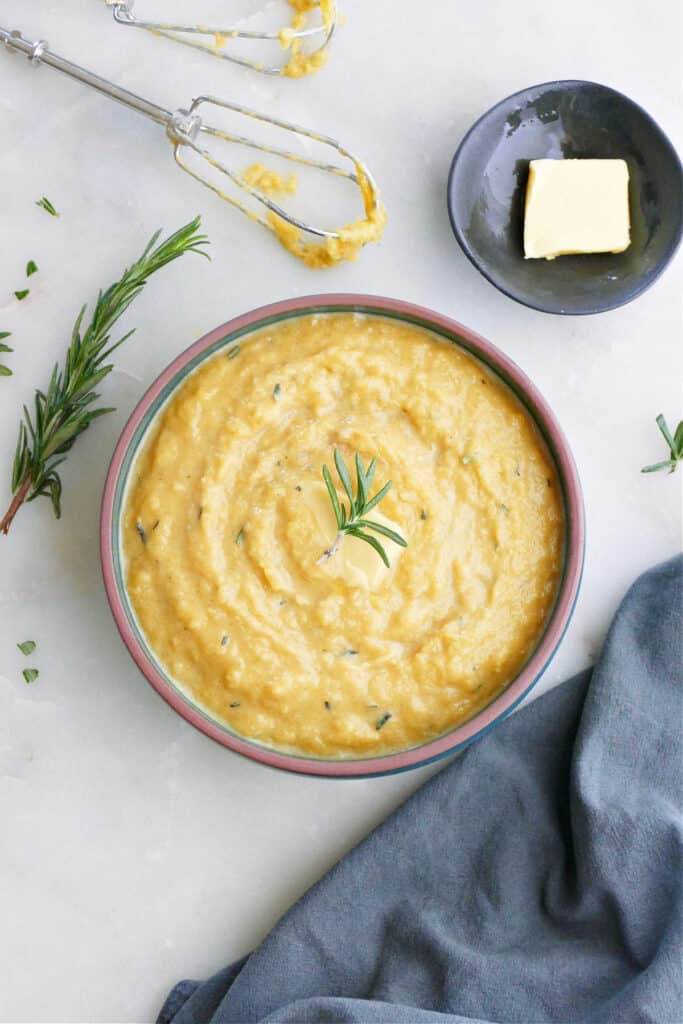 mashed acorn squash topped with rosemary in a bowl on a counter