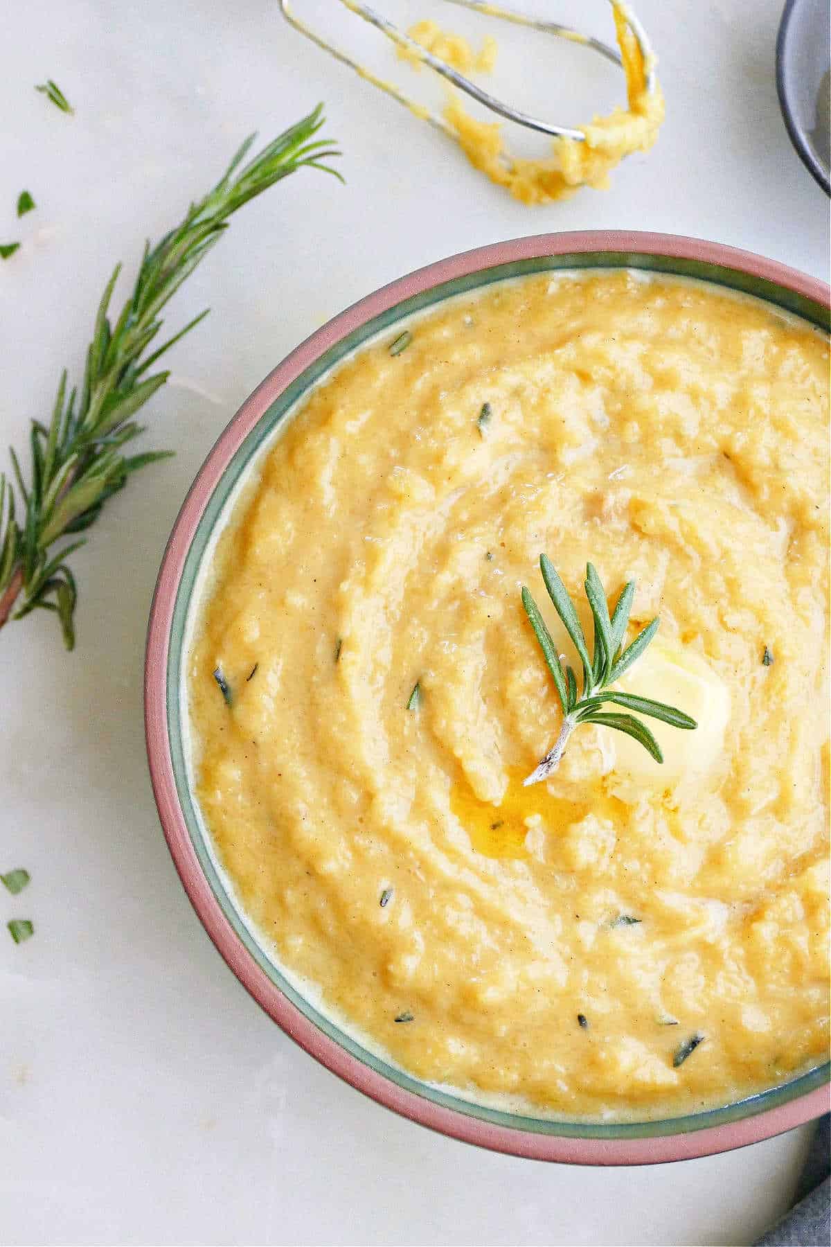 mashed acorn squash topped with rosemary in a serving bowl on a counter