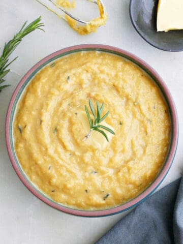 mashed acorn squash topped with rosemary in a bowl on a counter