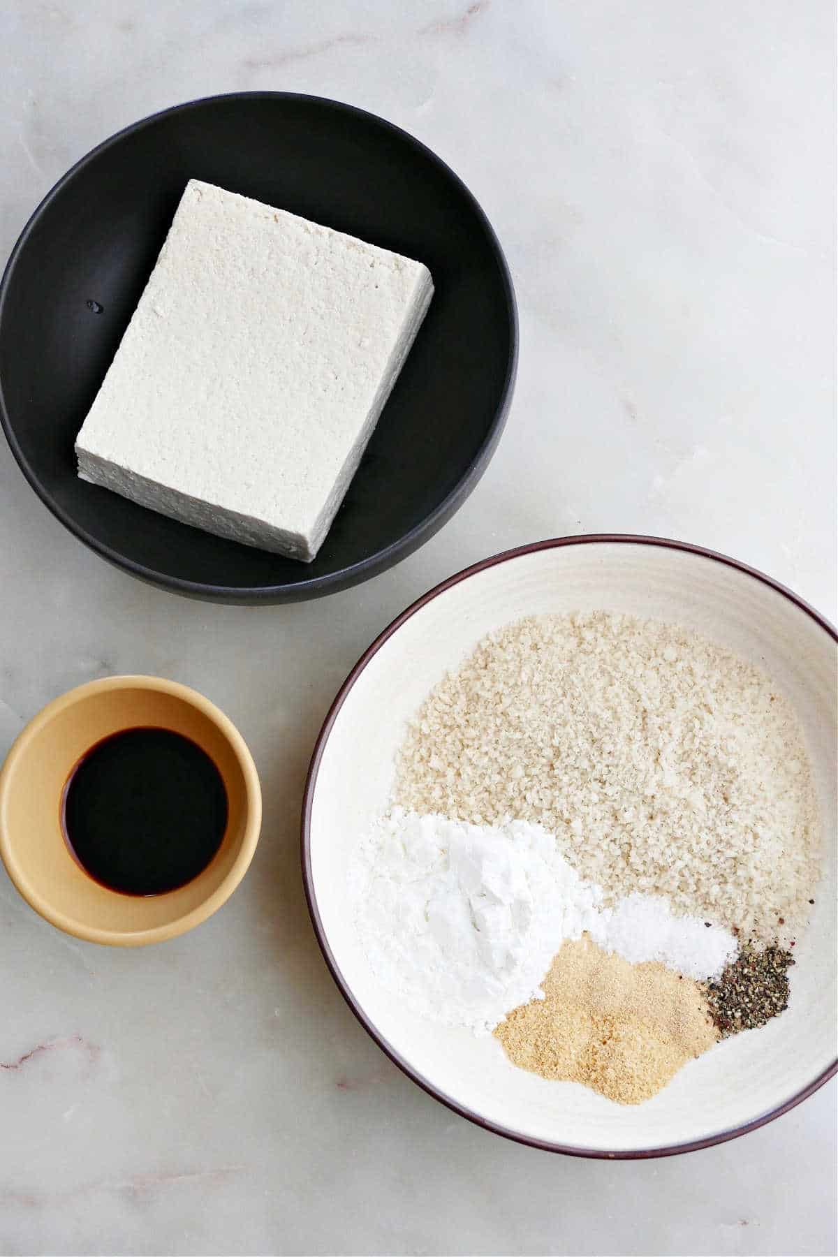 a block of tofu in a bowl next to bowls with breading ingredients