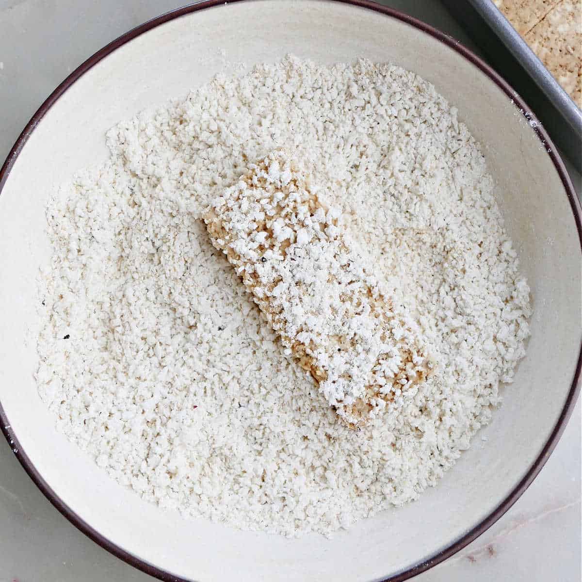 a piece of tofu pressed into panko breading in a bowl