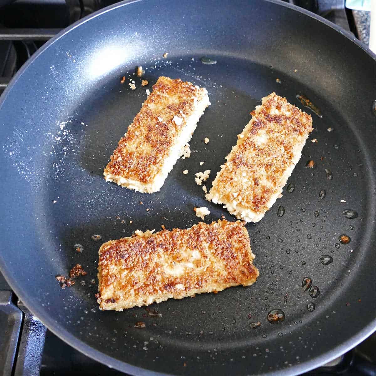 three pieces of panko tofu frying in a skillet