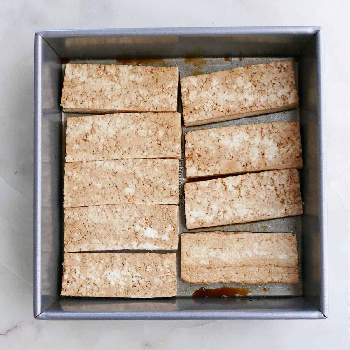 tofu pieces marinating in soy sauce in a square dish