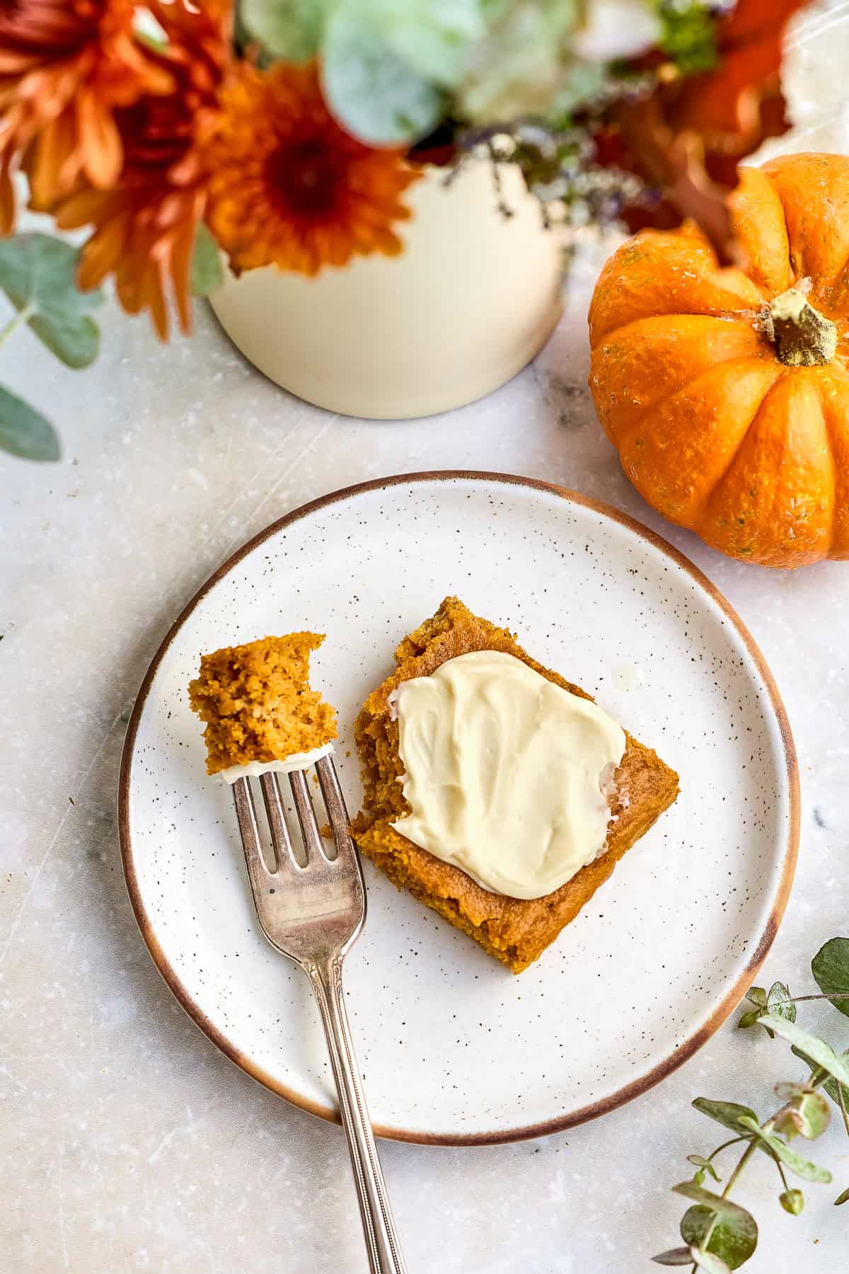 Pumpkin bar next to a fork with a bite on a plate surrounded by fall flowers.