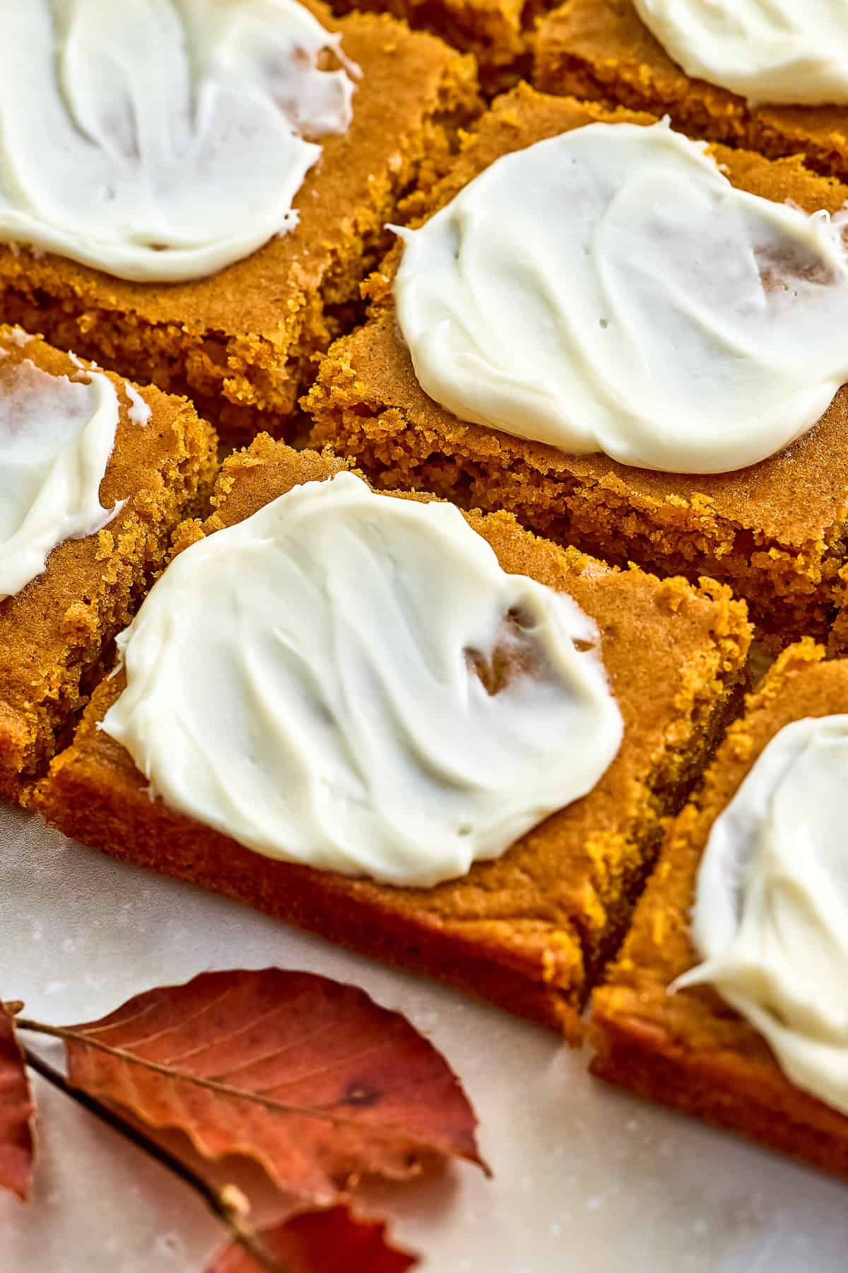 Sliced pumpkin cake bars with cream cheese frosting next to orange leaf.
