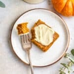 Frosted pumpkin bar next to a fork with a bite on a plate.