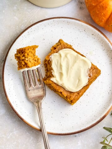 Frosted pumpkin bar next to a fork with a bite on a plate.