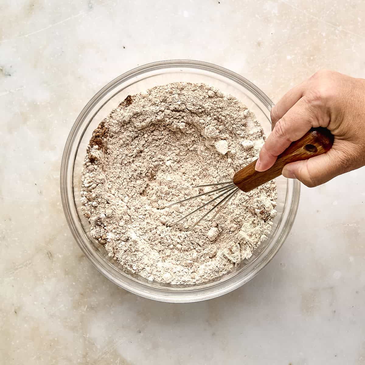 Woman whisking flours, spices, and dry ingredients in a large bowl.