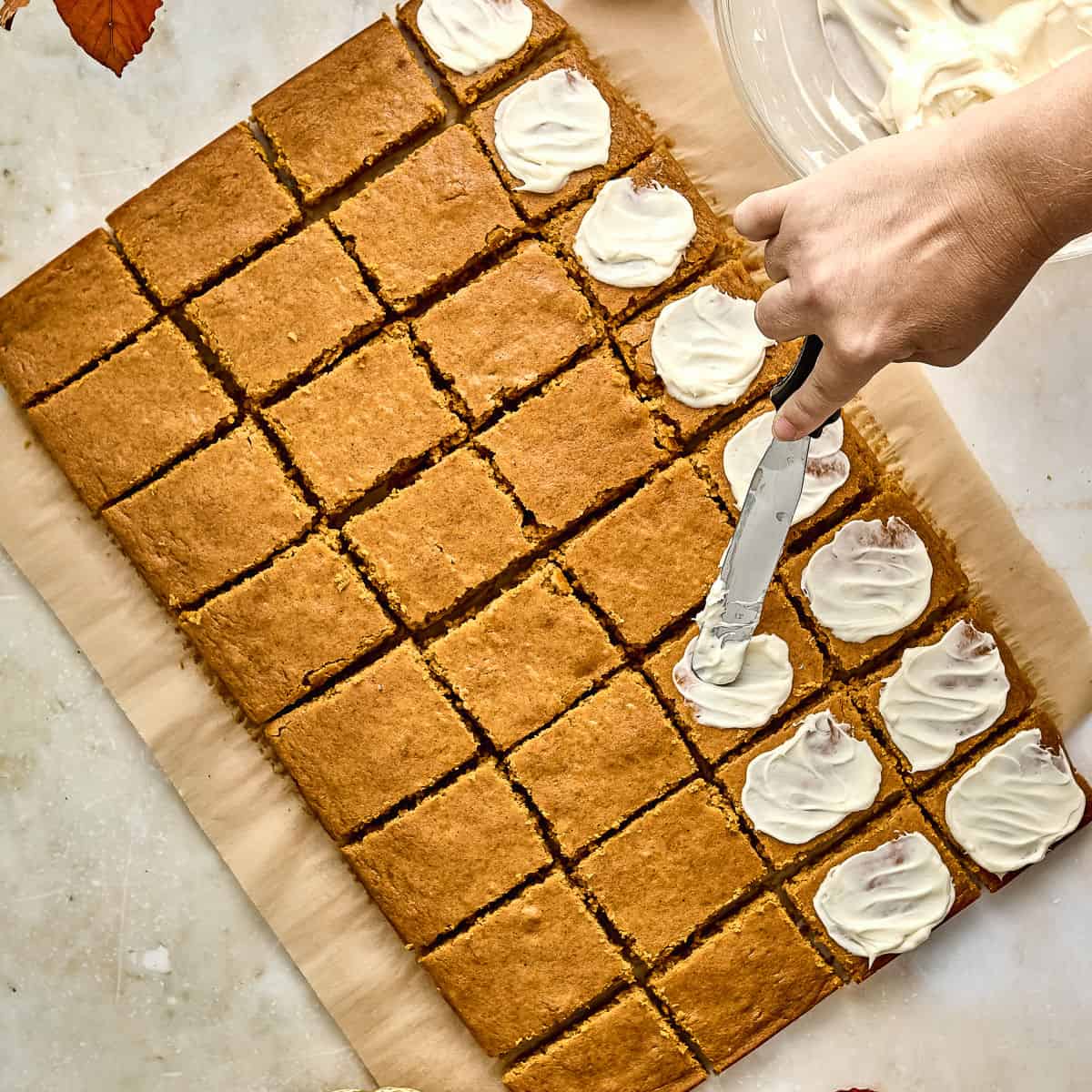 Woman spreading frosting on top of sliced sheet pan pumpkin bars.
