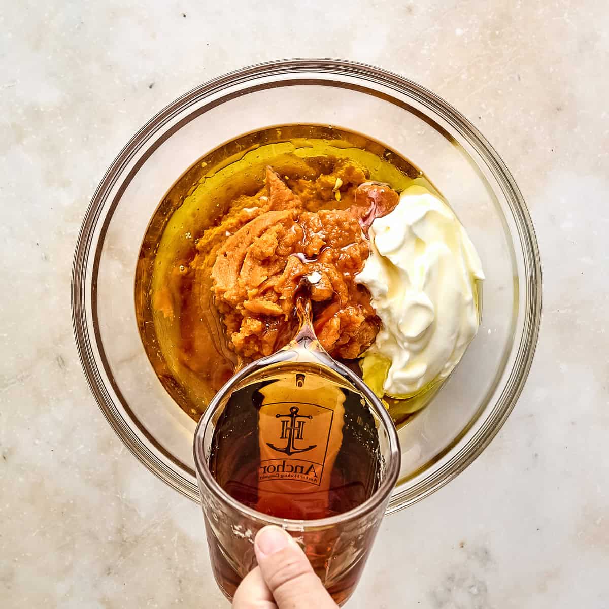 Woman pouring maple syrup into a bowl with pumpkin and Greek yogurt.