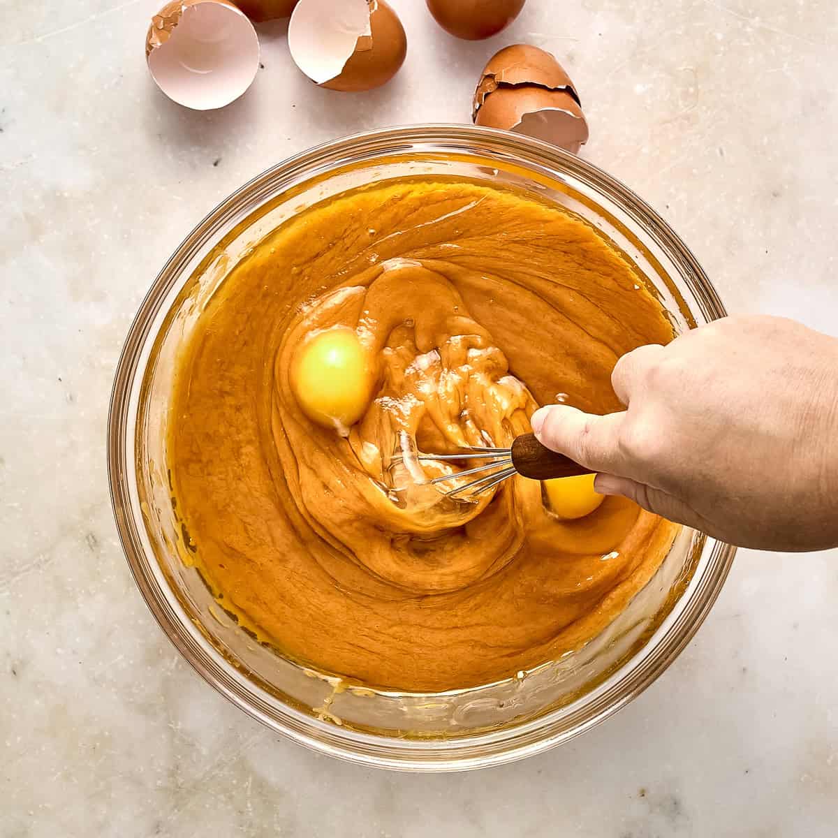 Woman whisking wet ingredients for pumpkin bars in a large glass bowl.