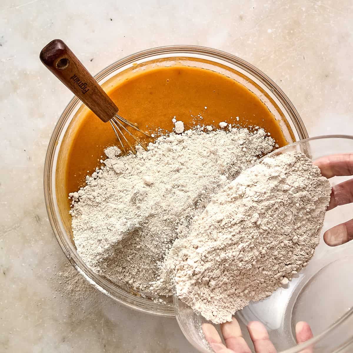 Woman adding dry ingredients for pumpkin bars to a bowl with wet ones.