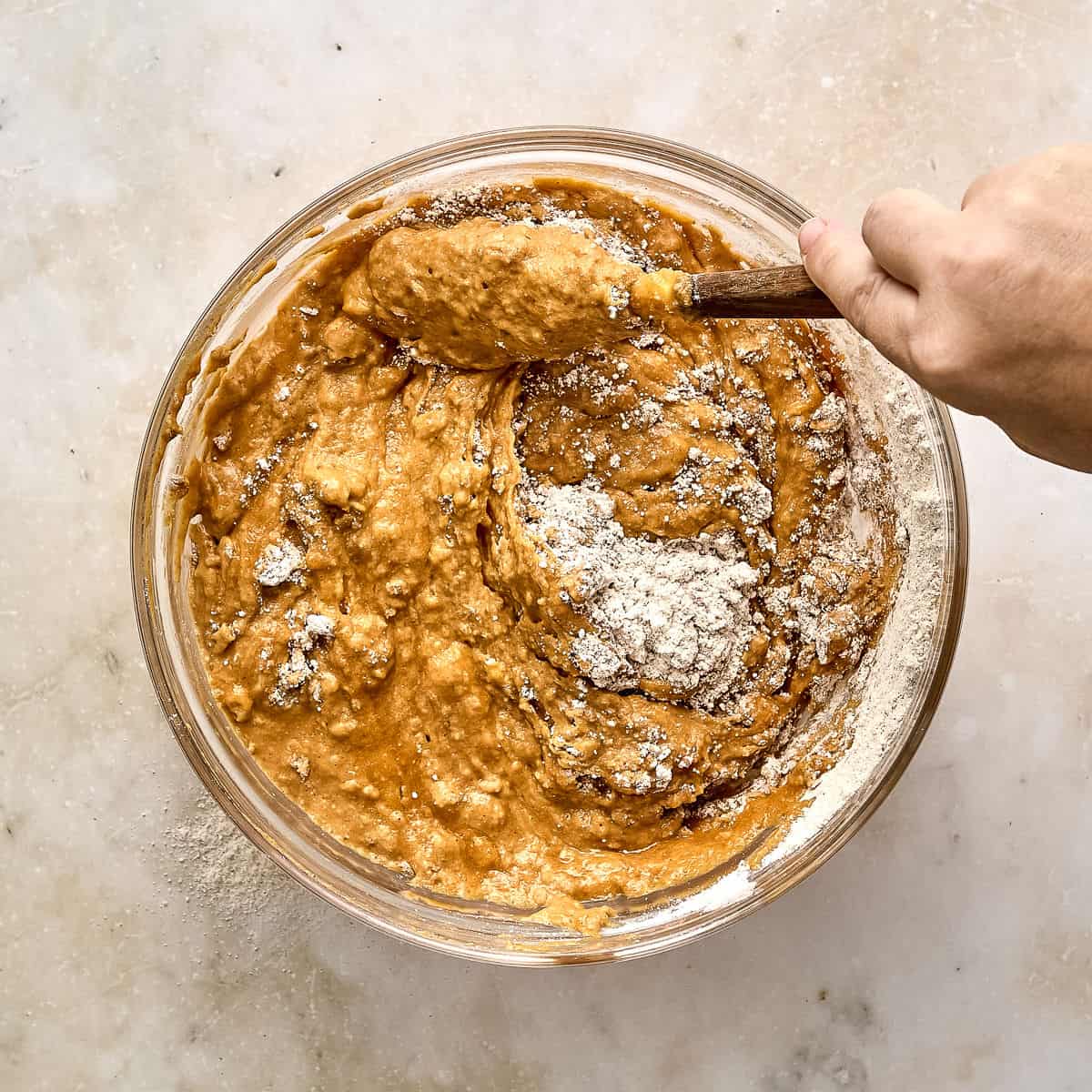 Woman stirring dry ingredients into wet batter for a pumpkin bar recipe.