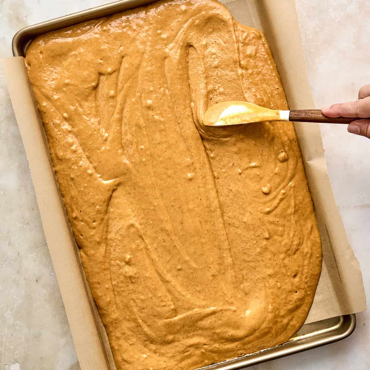 Woman spreading batter into a smooth layer on a lined sheet pan.
