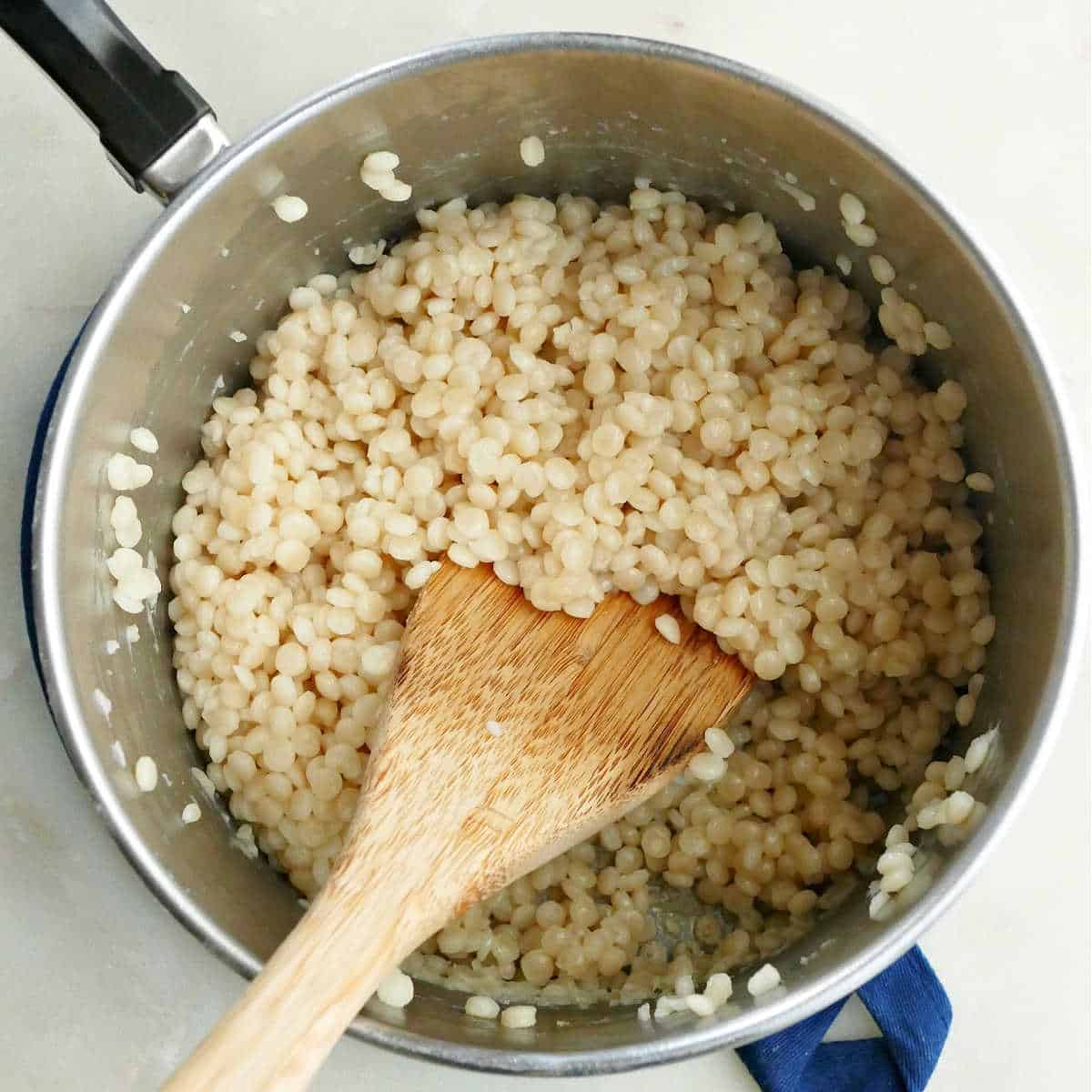 pearl couscous cooking in a saucepan with a wooden spoon