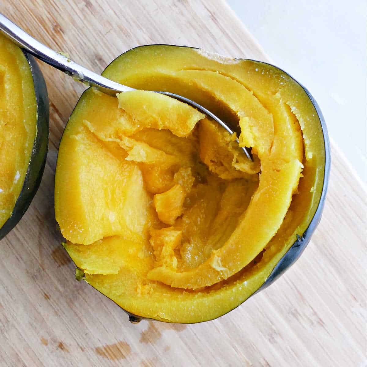 cooked acorn squash with a spoon scooping out the flesh