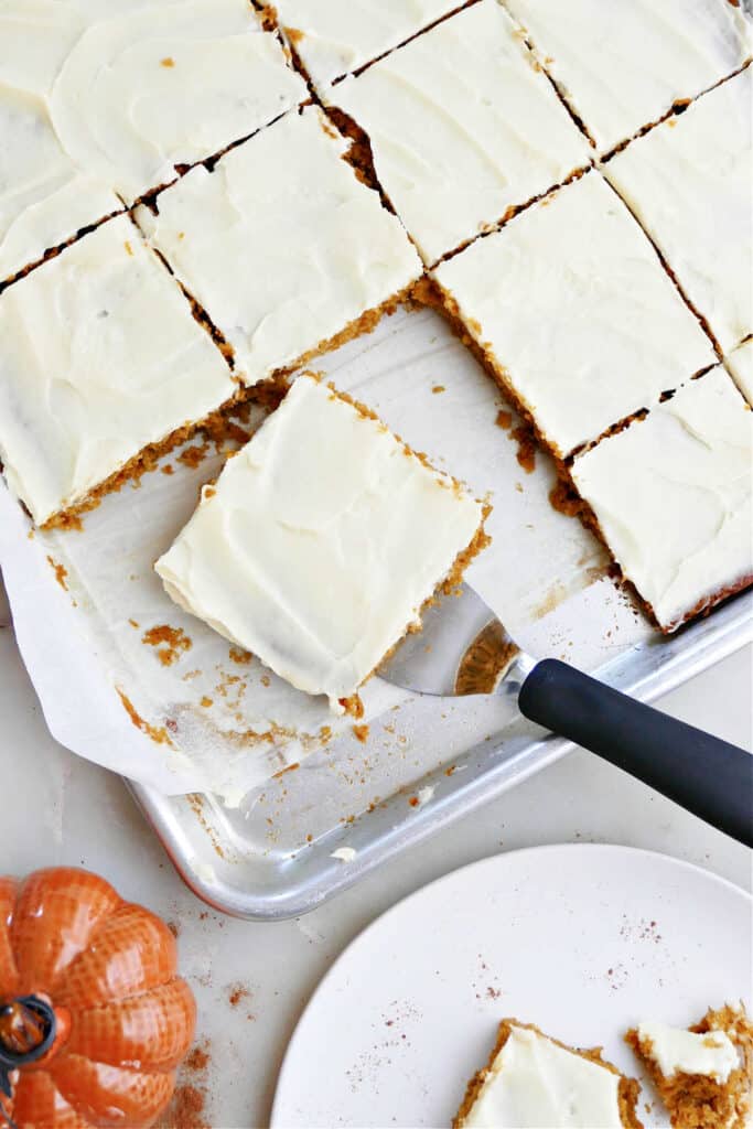 sheet pan of pumpkin bars with frosting and a spatula picking up one bar