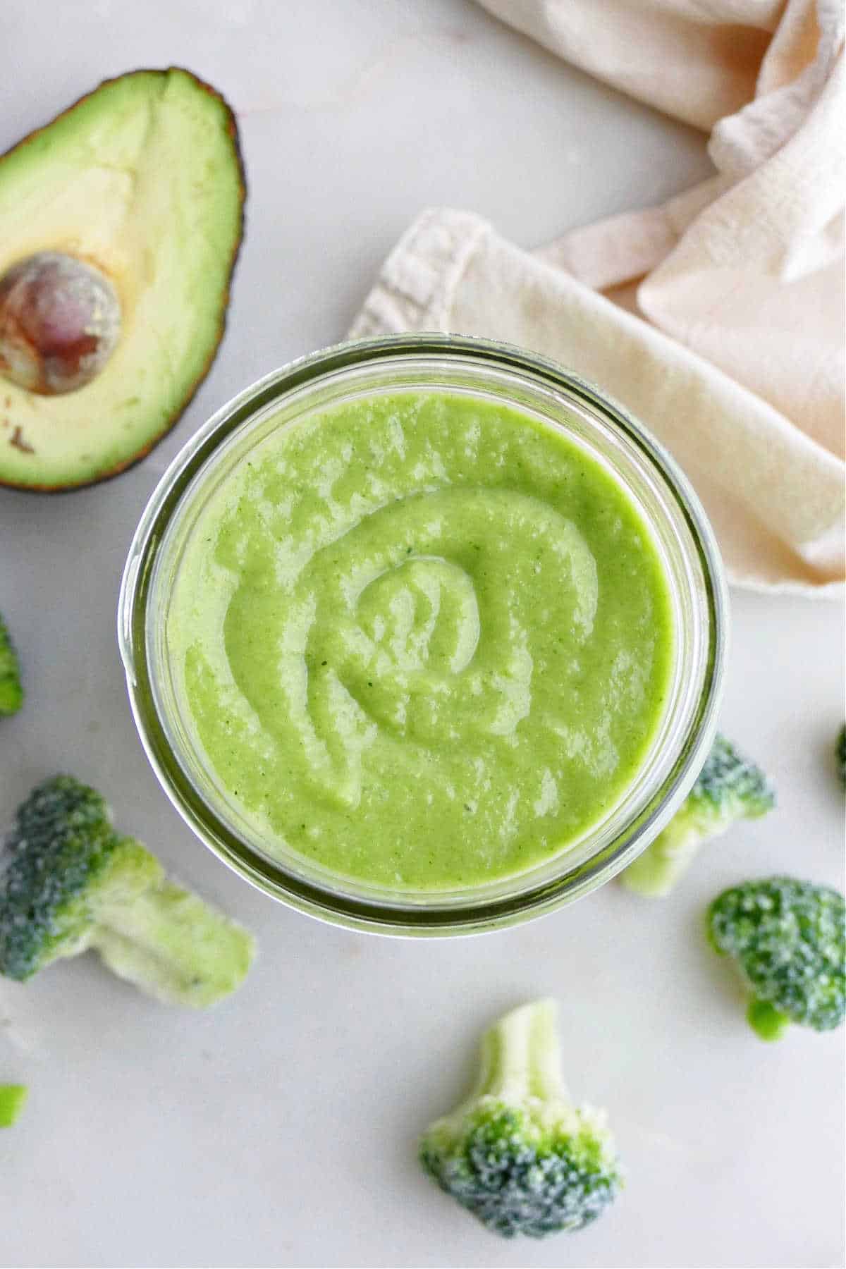 broccoli smoothie in a glass on a counter next to avocado and broccoli