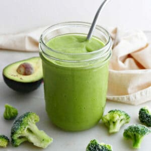 broccoli smoothie in a glass with a steel straw surrounded by ingredients