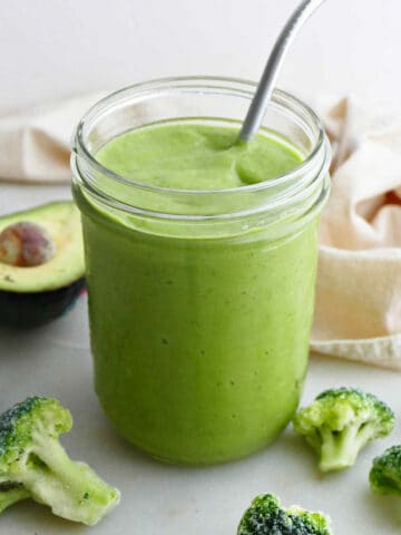 broccoli smoothie in a glass with a steel straw surrounded by ingredients