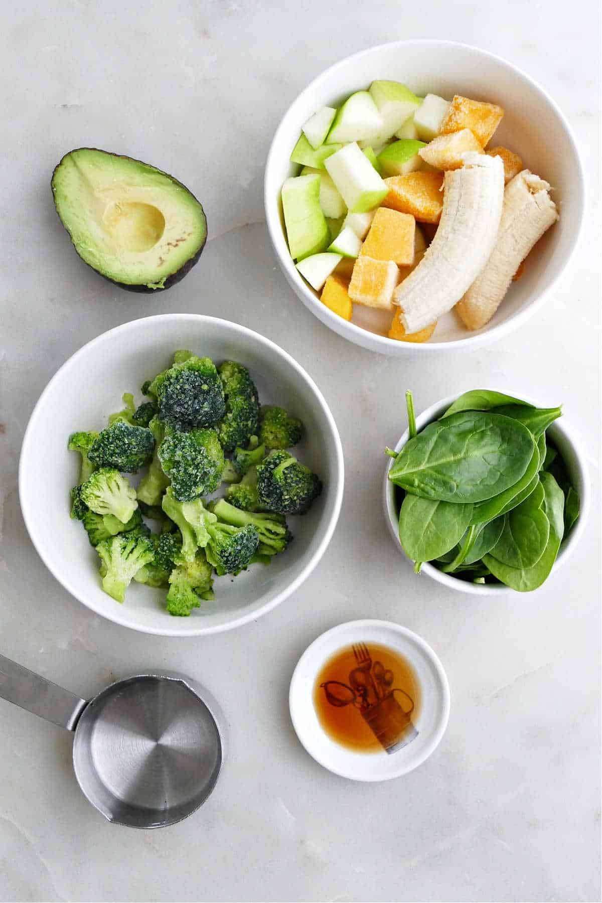 avocado, fruit, frozen broccoli, spinach, vanilla extract, and water on a counter