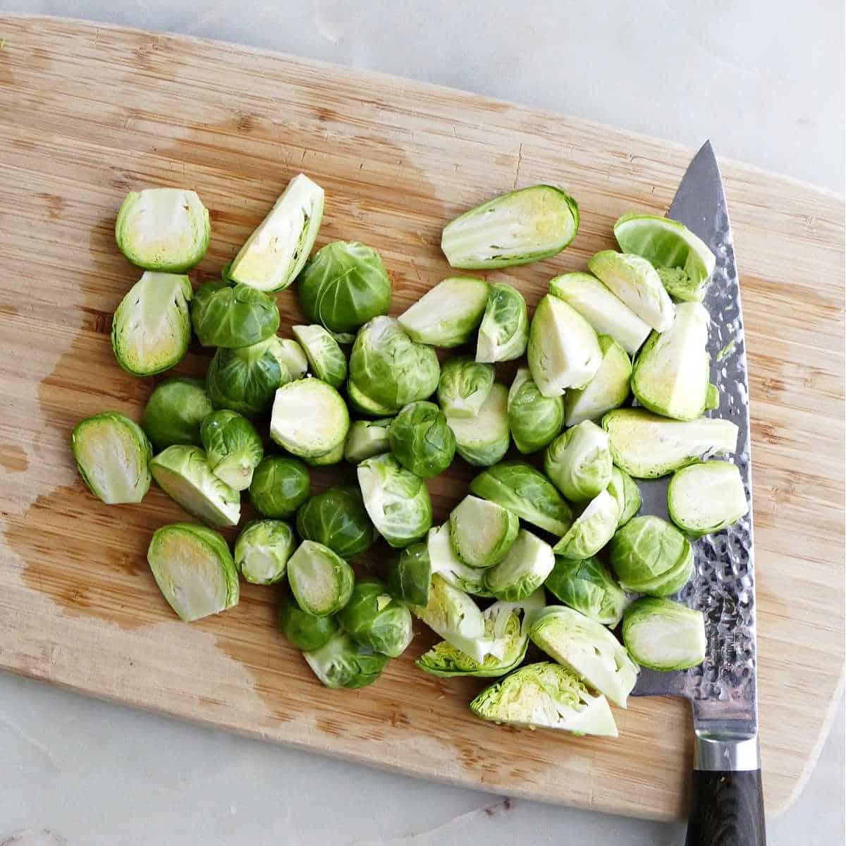 Brussels sprouts being sliced in half on a cutting board