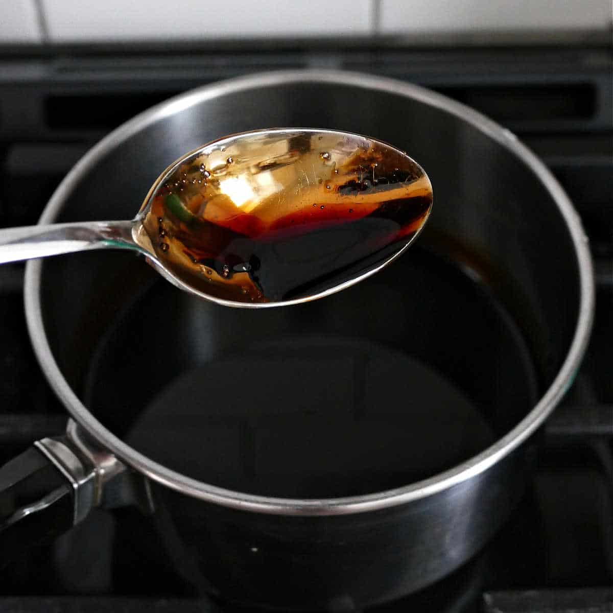 spoon with balsamic maple glaze over a saucepan cooking on a stove