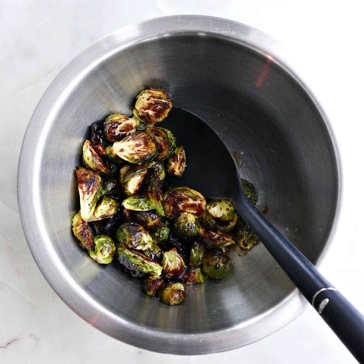 roasted Brussels sprouts being tossed in a balsamic maple glaze in a bowl