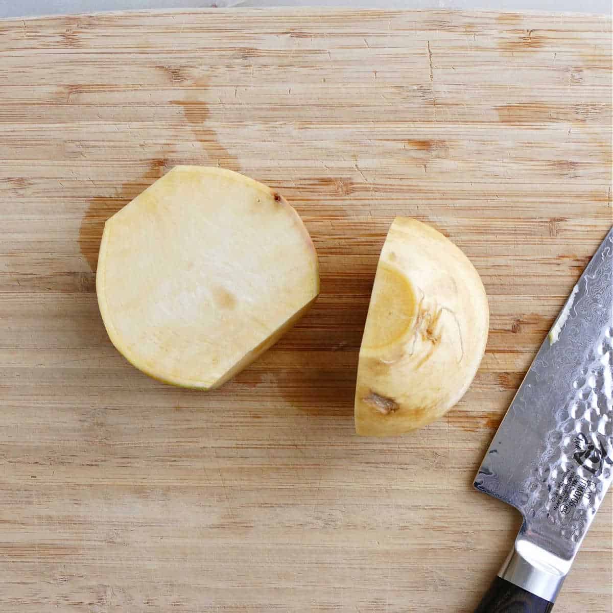 rutabaga cut in half with a knife on a bamboo cutting board