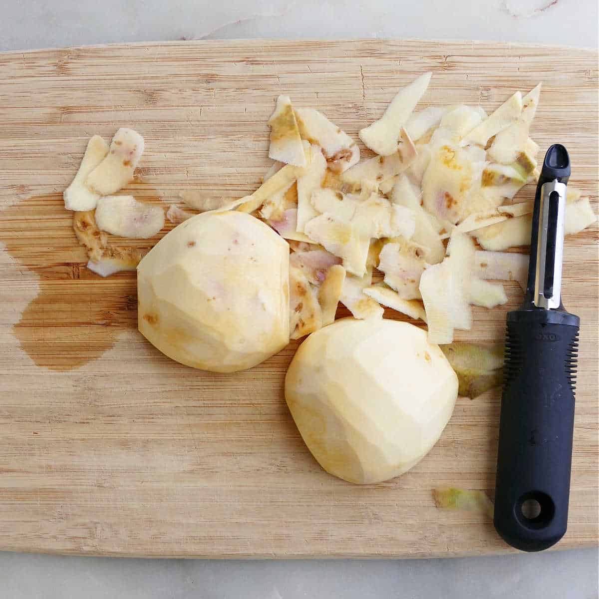two halves of rutabaga peeled with a swivel peeler on a bamboo cutting board