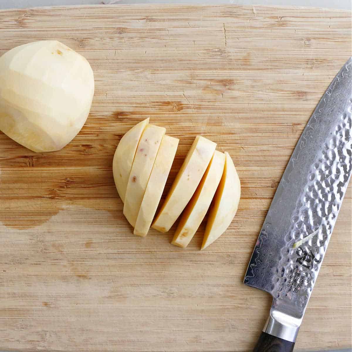 rutabaga cut into slices with a knife on a bamboo cutting board