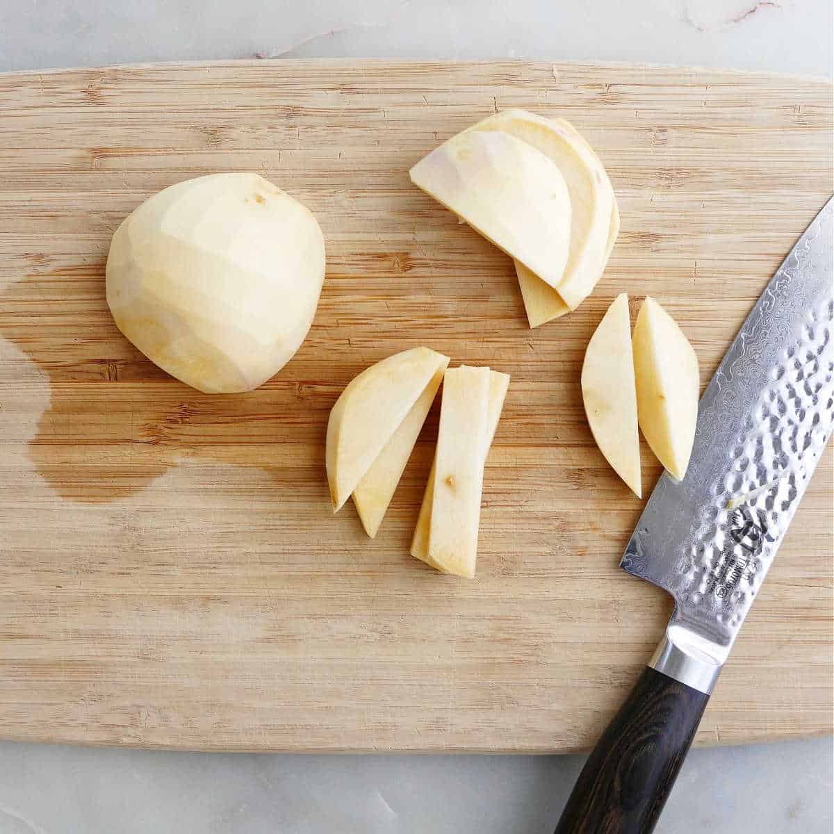 rutabaga being sliced into fries with a knife on a cutting board
