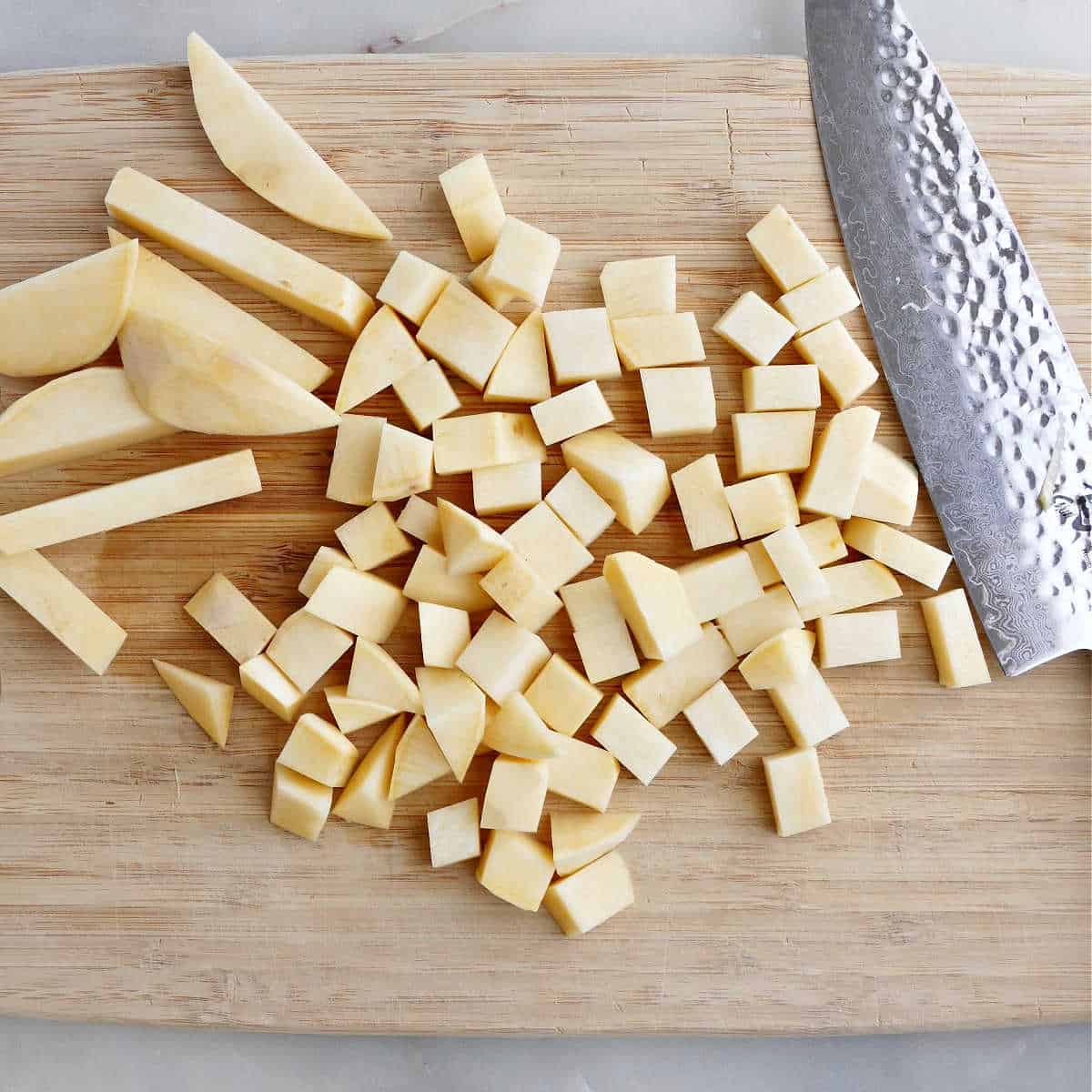 rutabaga being sliced into cubes with a knife on a cutting board