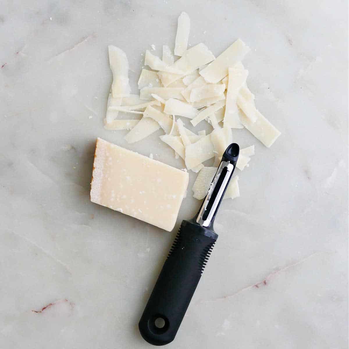 block of parmesan with shavings next to a swivel peeler