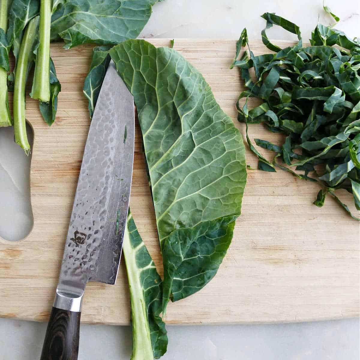 stems of collard greens being sliced off on a cutting board