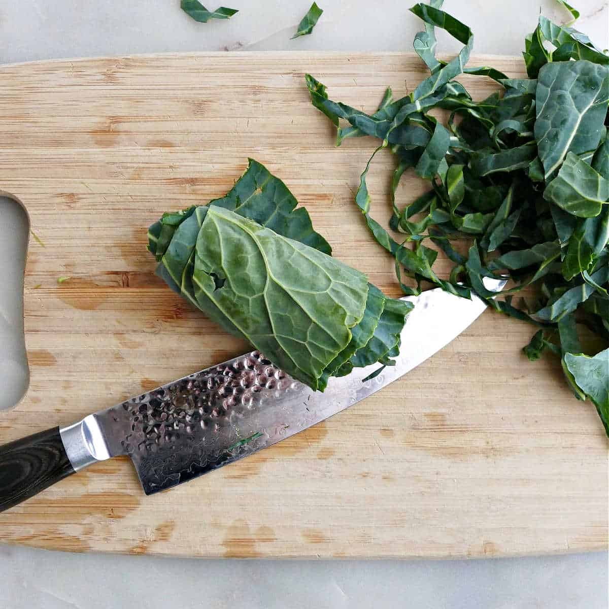 collard greens rolled up on a cutting board with a knife