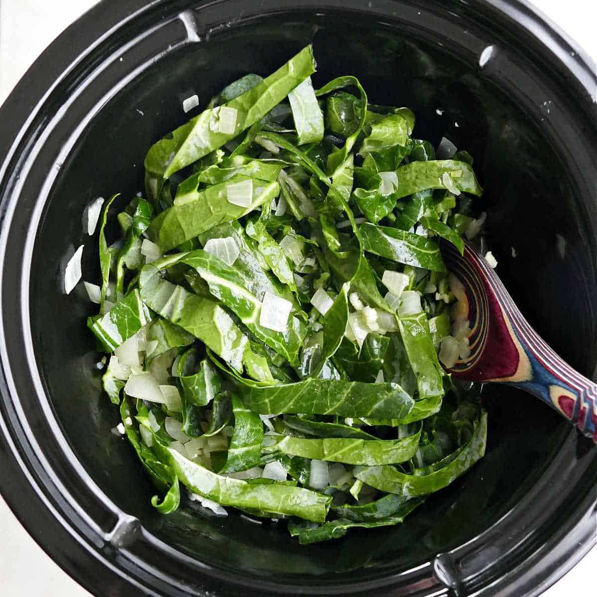 collard greens and onions cooking in broth in a slow cooker