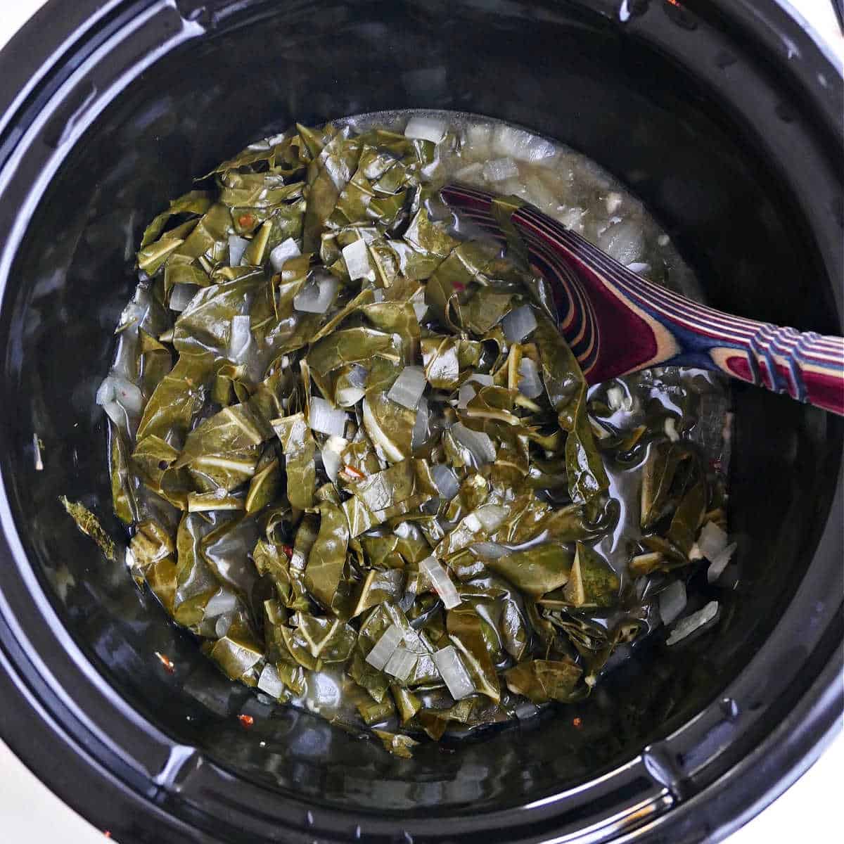 cooked collard greens in a slow cooker with a serving spoon
