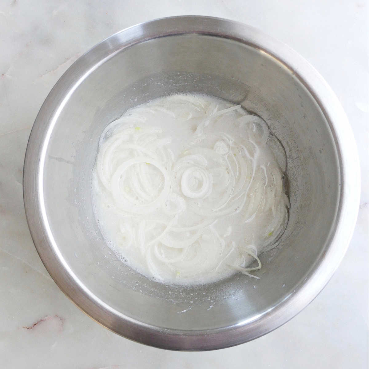 thinly sliced onions soaking in almond milk and vinegar in a bowl