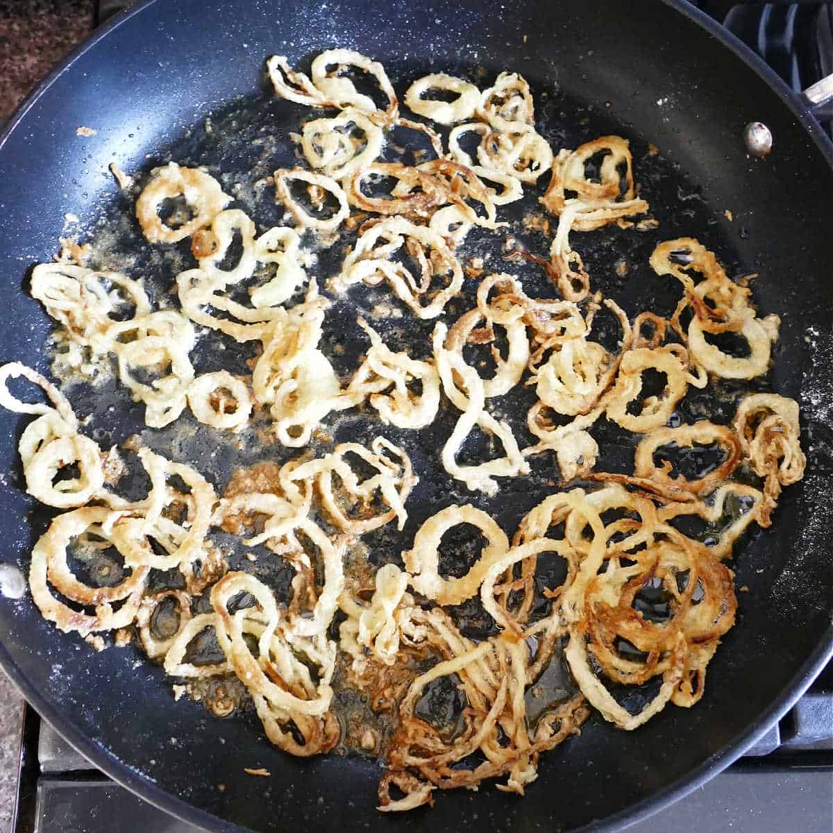 crispy onions cooking in oil in a large skillet