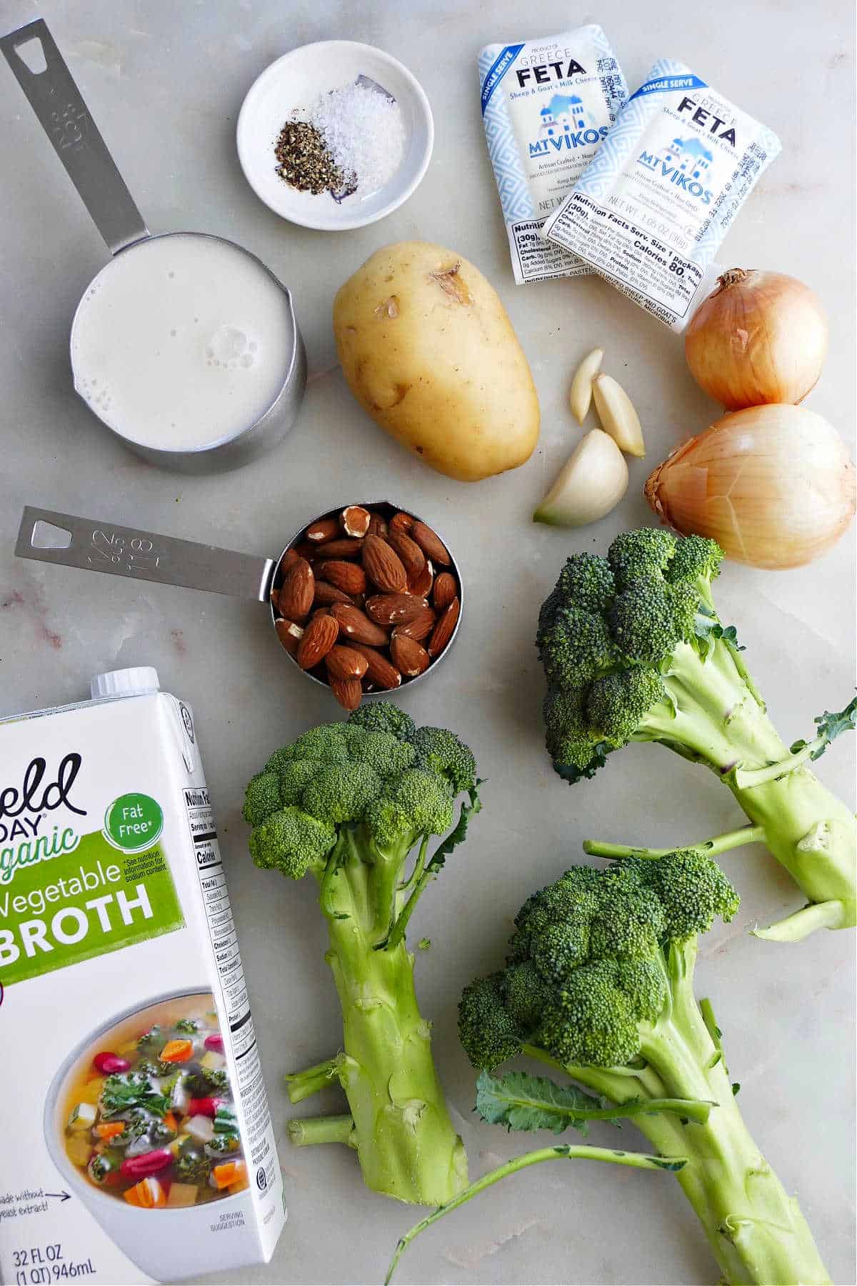 almond milk, potato, feta, onions, spices, broccoli, almonds, and broth on a counter