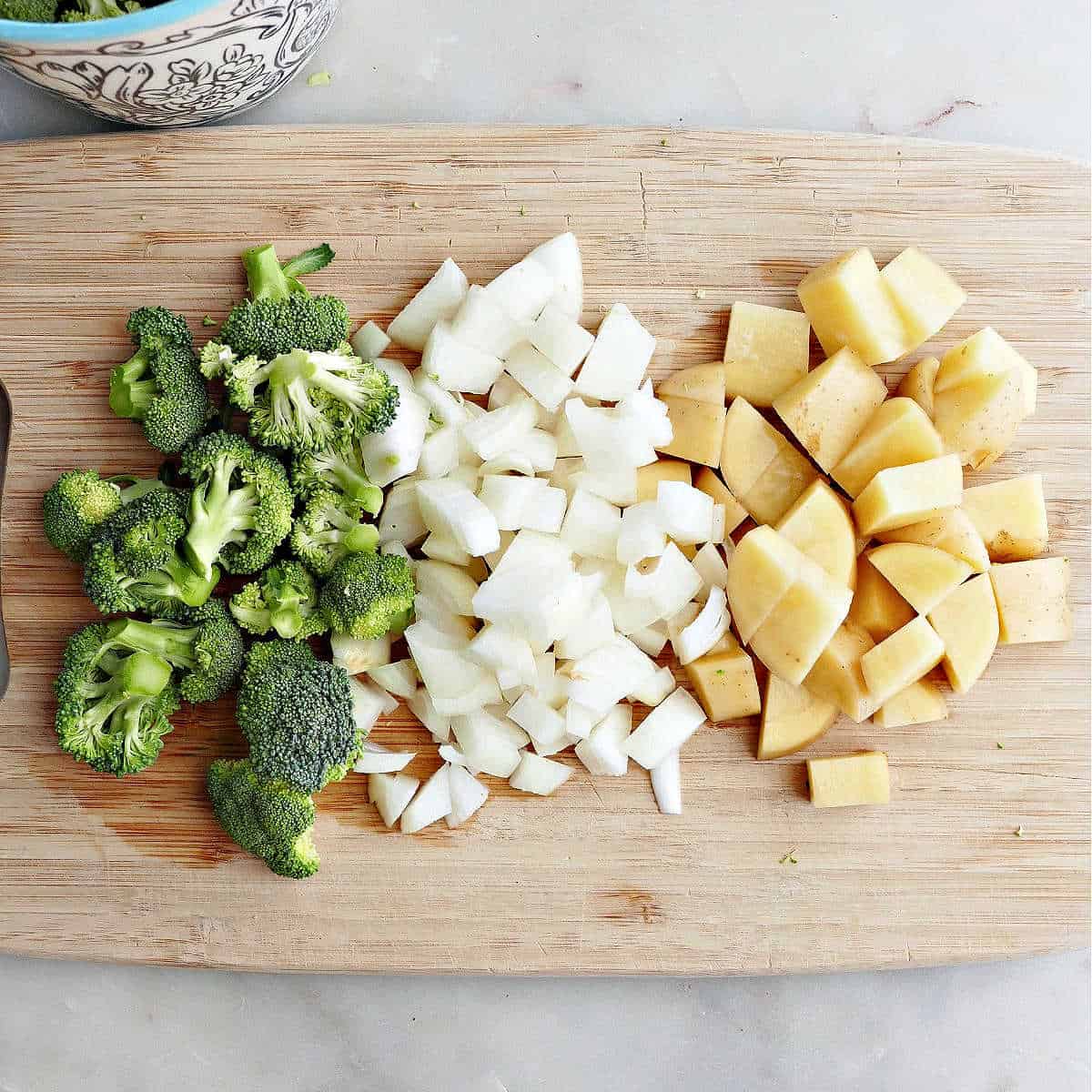 chopped broccoli, onion, and potato on a bamboo cutting board on a counter
