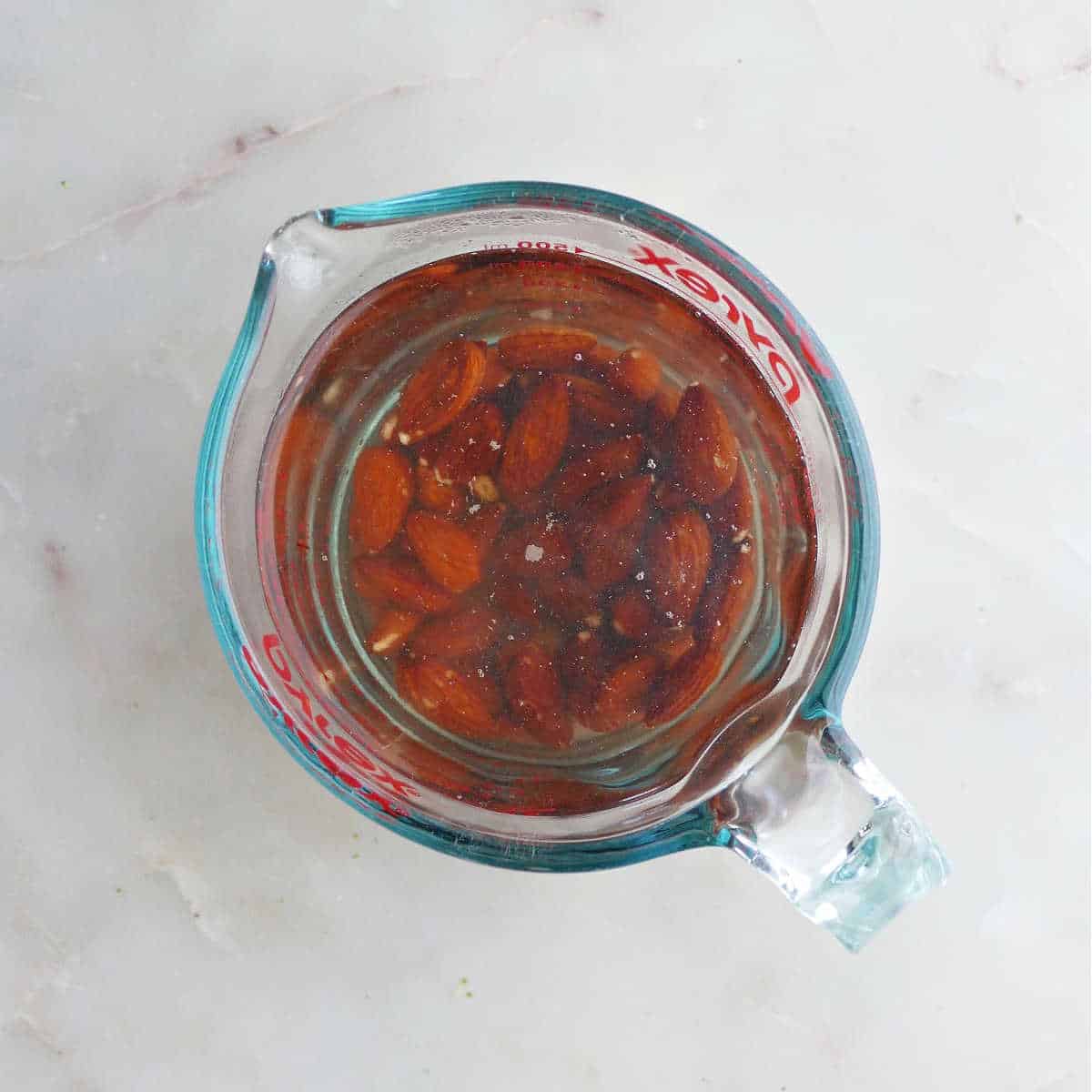 almonds soaking in boiling water in a measuring cup on a counter