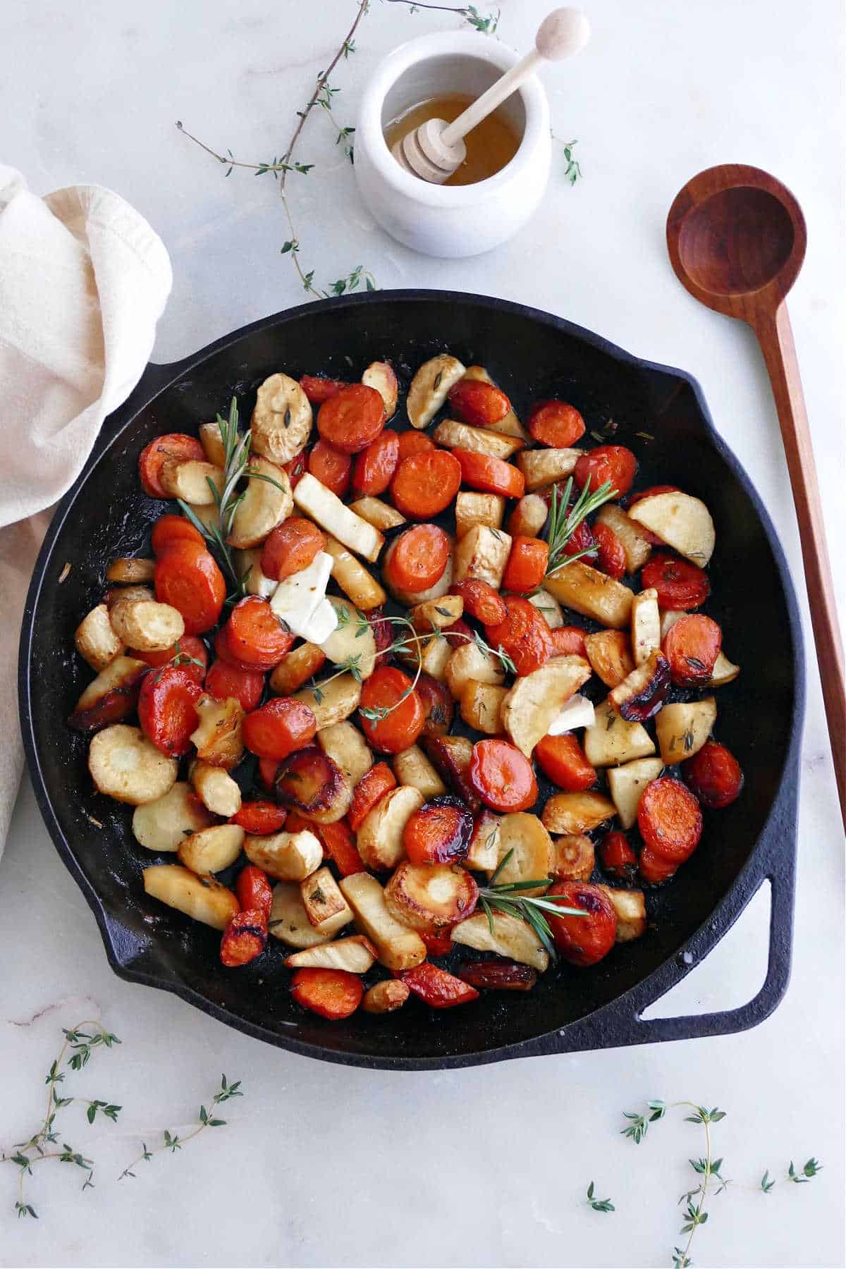 roasted carrots and parsnips with honey and herbs in a cast iron pan on a counter