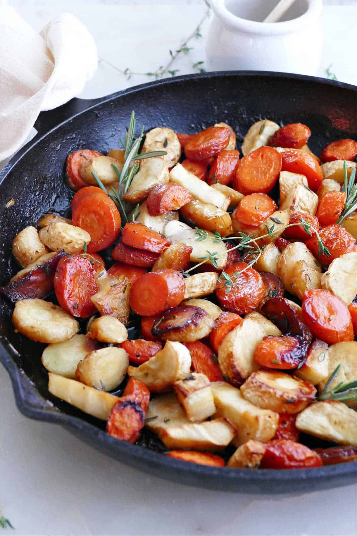 roasted carrots and parsnips with honey and herbs in a cast iron pan on a counter