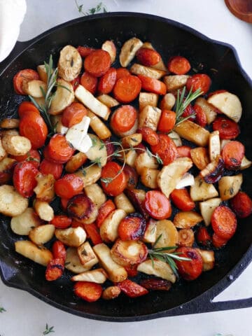 roasted carrots and parsnips with honey and herbs in a cast iron pan on a counter