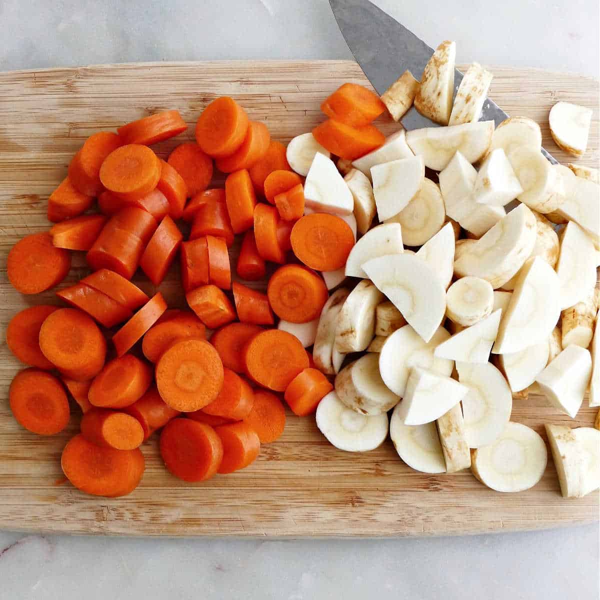 sliced carrot and parsnip coins on a bamboo cutting board with a knife