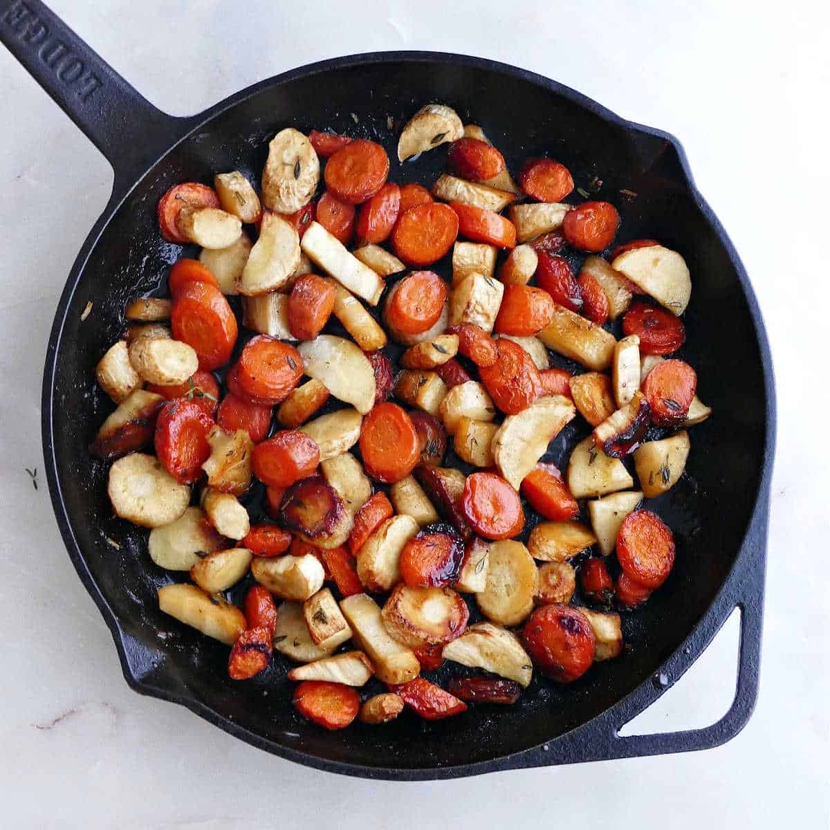 roasted root vegetables and herbs in a cast iron pan after being roasted